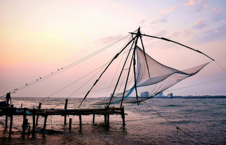 A traditional Chinese fishing net structure stands majestically over calm waters during a serene sunset or sunrise. The iconic cantilever fishing system