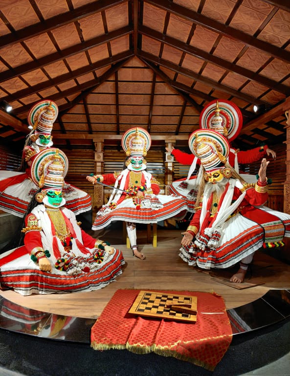 This image captures a traditional Kathakali performance scene from Kerala, India, featuring four performers in elaborate costumes and makeup. The dancers wear